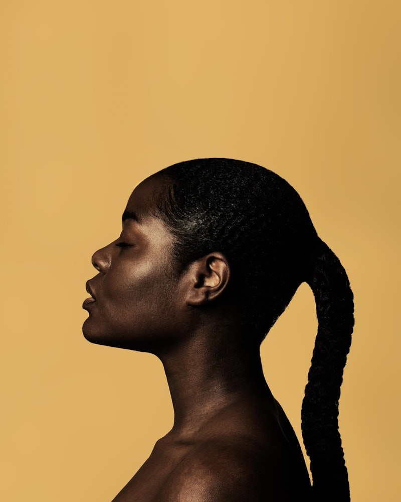 High-fashion profile of Black woman with sleek silk-pressed ponytail on warm studio background